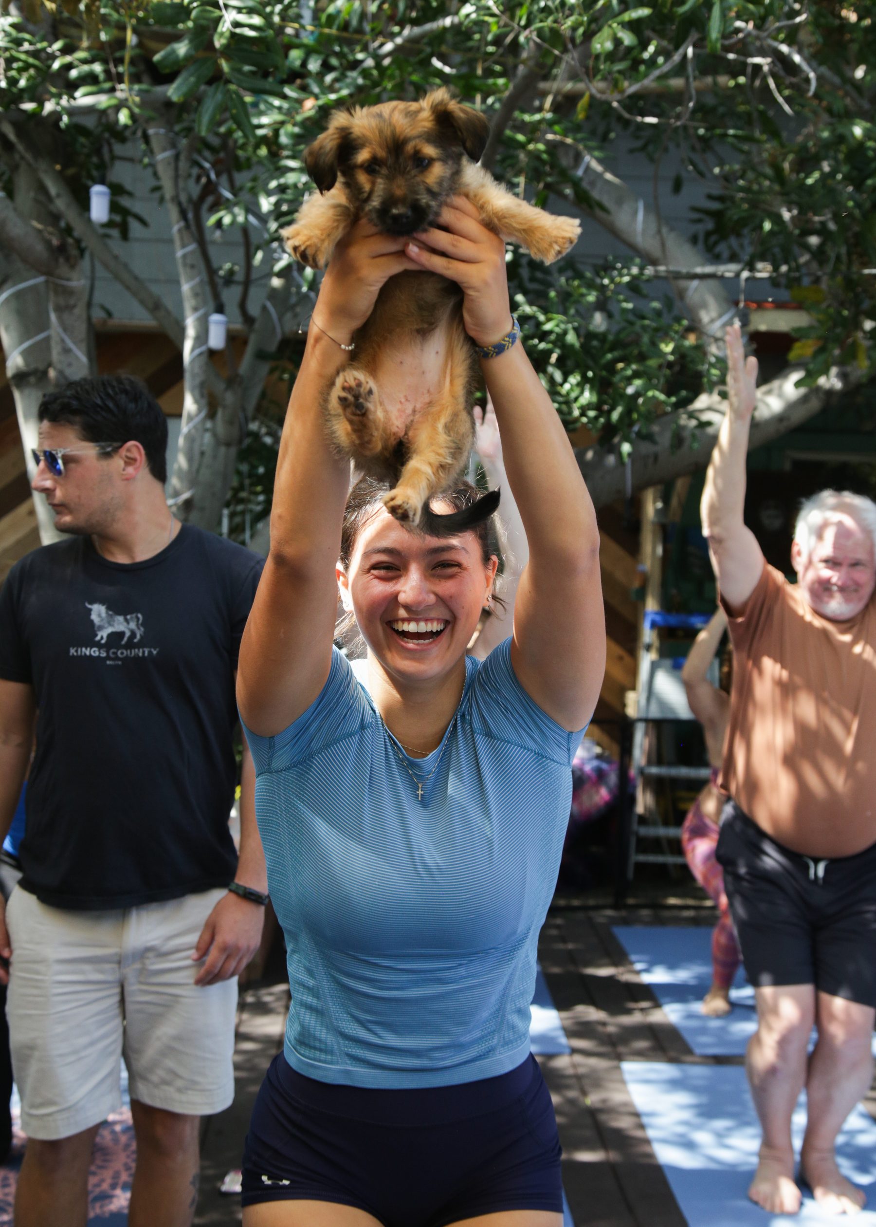 A guest holds an adoptable puppy overhead, full-body smile, Bark n Burn class in Ocean Beach